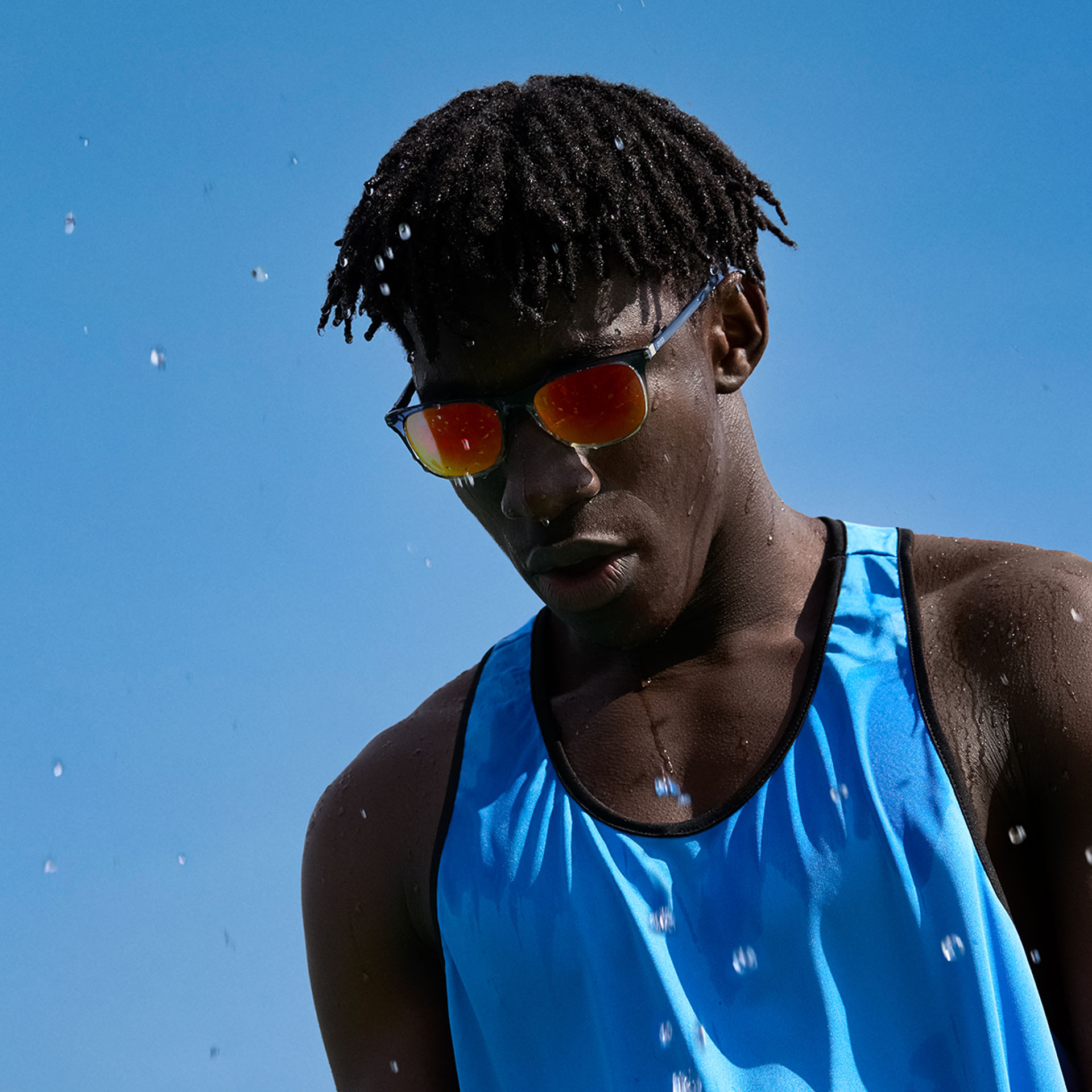 Joven con ropa deportiva y lentes solares de alto rendimiento de ZEISS en tono marrón anaranjado ante un cielo azul.
