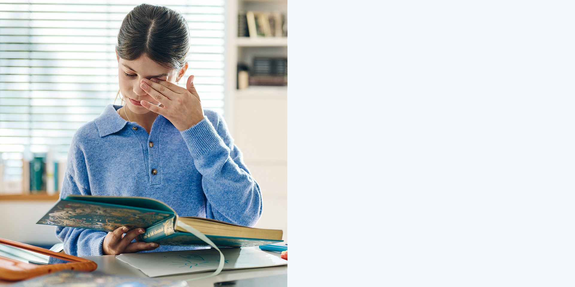 Joven de cabello castaño sin gafas frotándose los ojos mientras lee un libro.