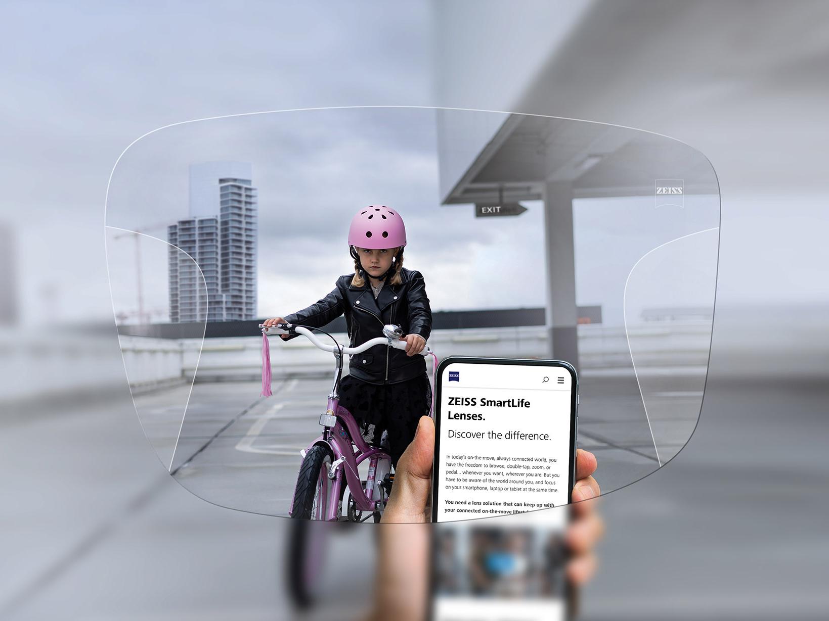 Una persona consulta su teléfono a través de los lentes progresivos ZEISS SmartLife. De fondo se puede ver a una niña con un casco rosa en una bicicleta. 