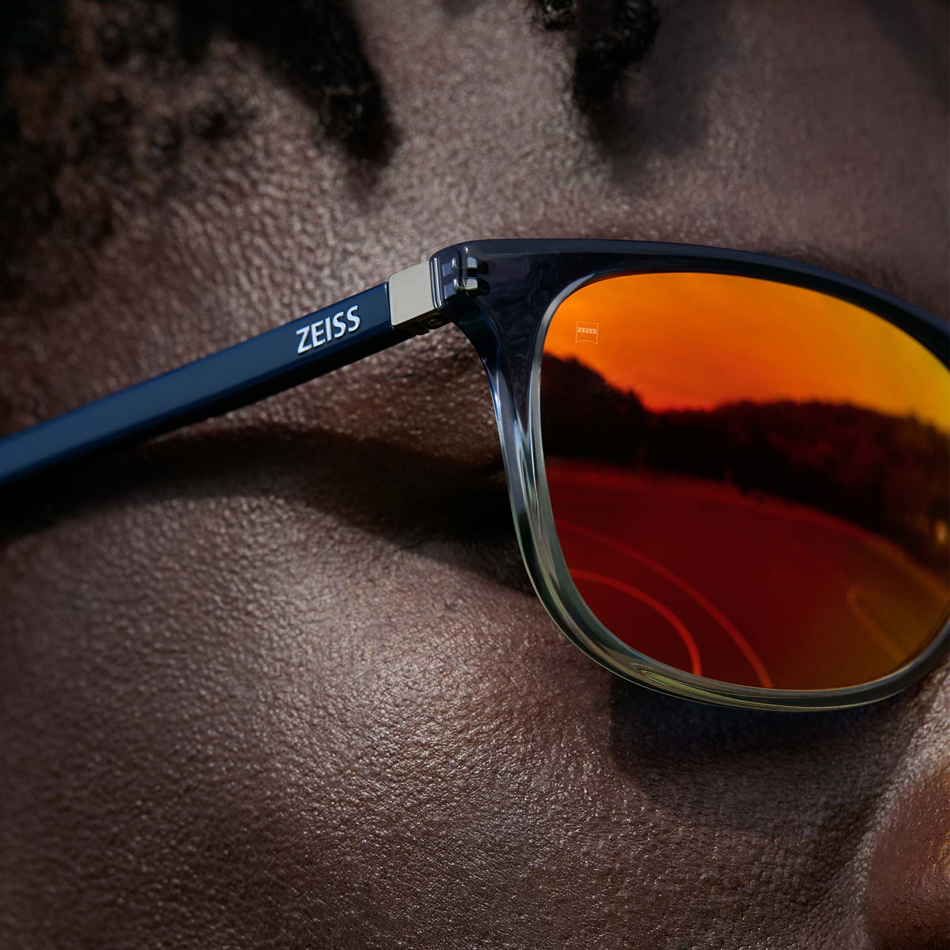 Primer plano de un hombre con lentes ZEISS Eyewear con recubrimiento solar ZEISS DuraVision Mirror UV en color naranja.
