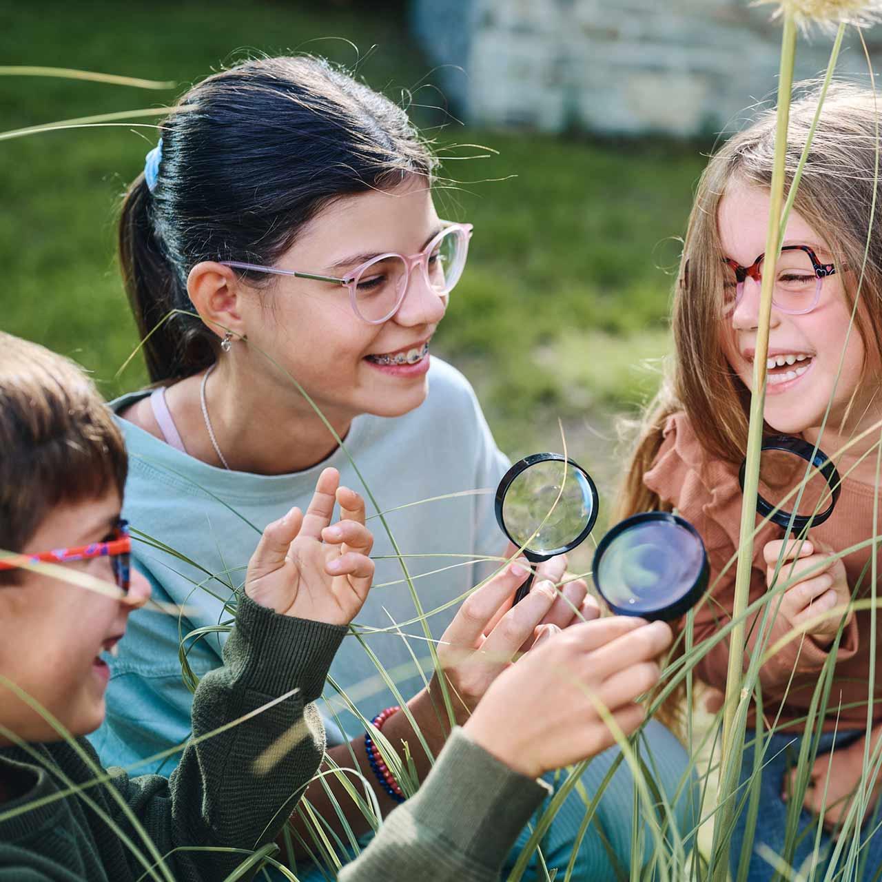 Grupo de niños con lentes y lupas jugando y riendo al aire libre