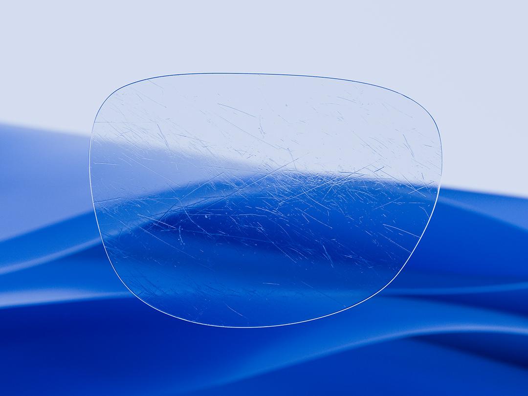 Imagen dividida que muestra un lente ZEISS en una mitad, caracterizado por su nitidez y limpieza, y un lente convencional rayado en la otra mitad, lo que resalta el contraste en relación con la durabilidad. 