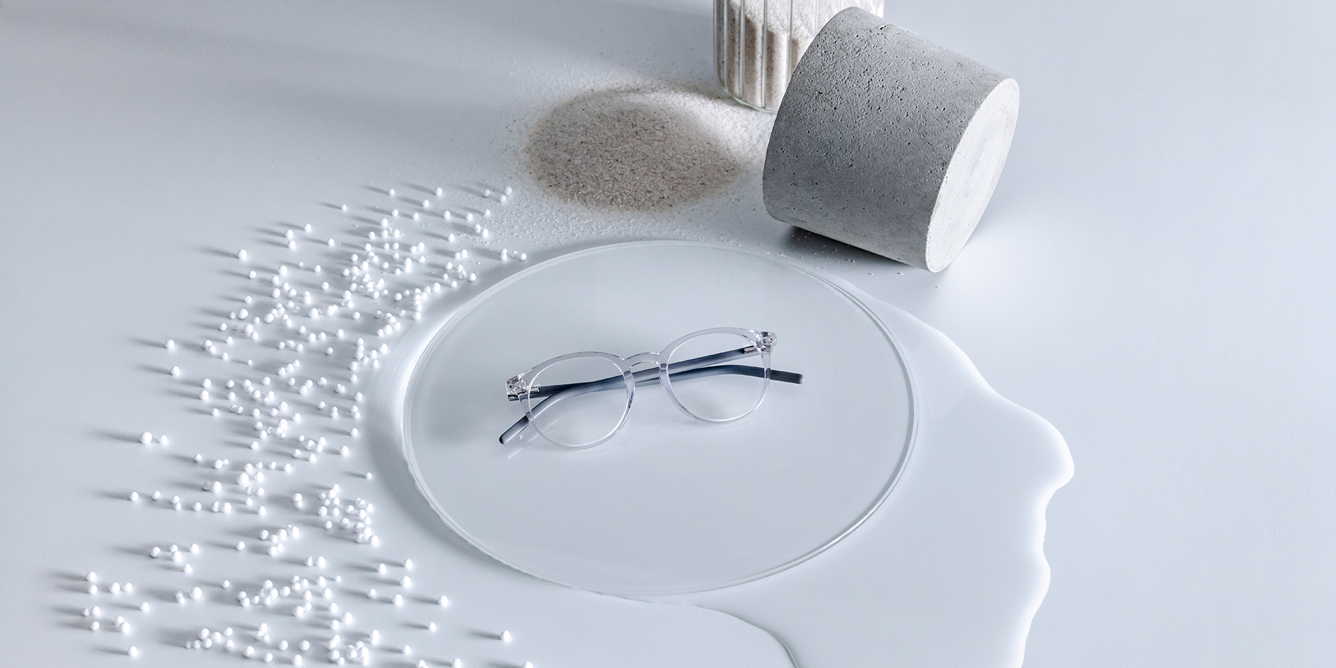 Lentes ZEISS con recubrimiento DuraVision® sobre un pedestal de cristal rodeado de agua, arena, perlas y piedra.