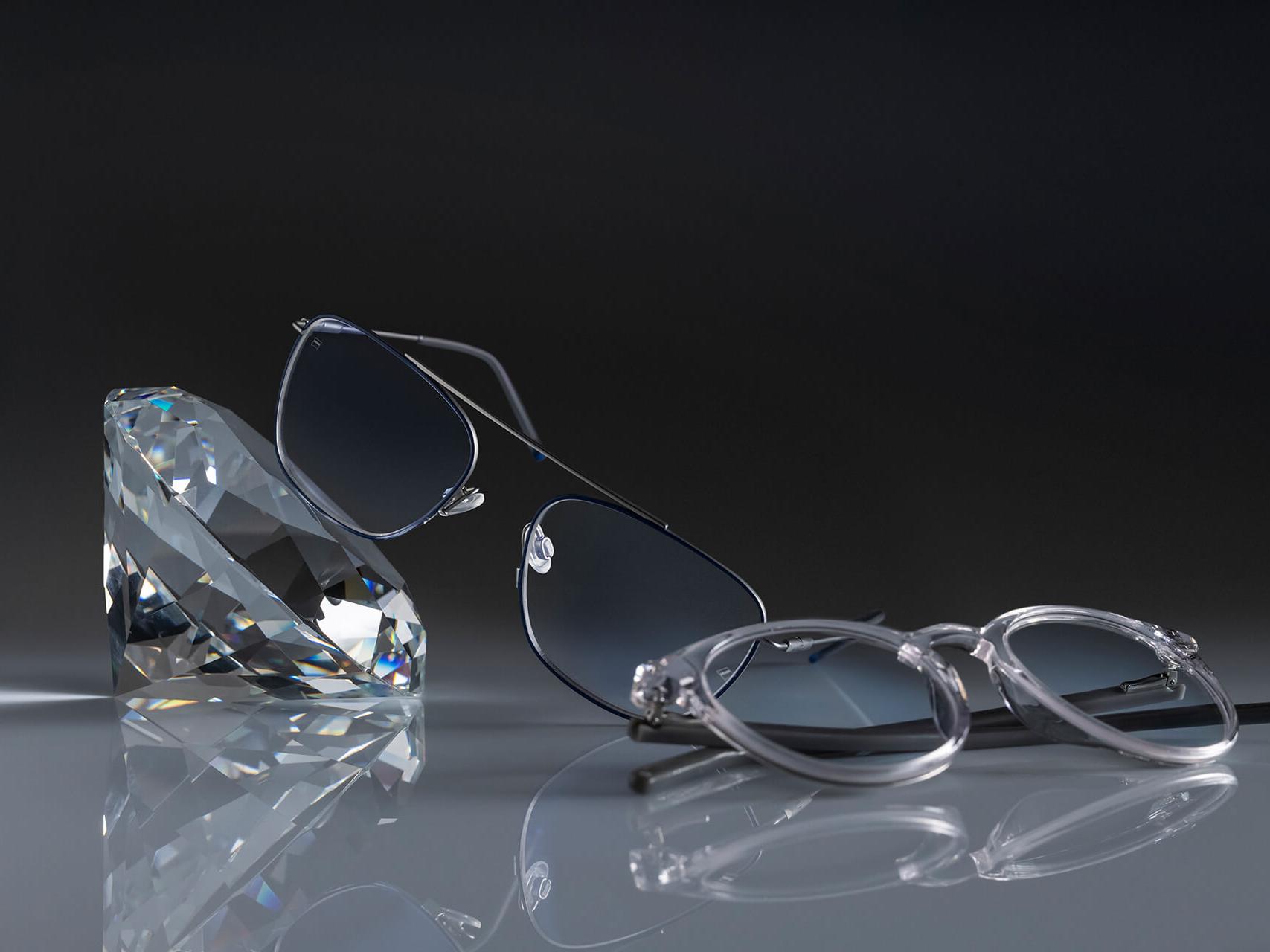 Dos pares de lentes ZEISS y el recubrimiento ZEISS más duro jamás visto: DuraVision® Platinum. Un par de lentes apoyado en un cristal, el otro sobre el suelo. Ambos tienen lentes transparentes sin reflejos azulados.