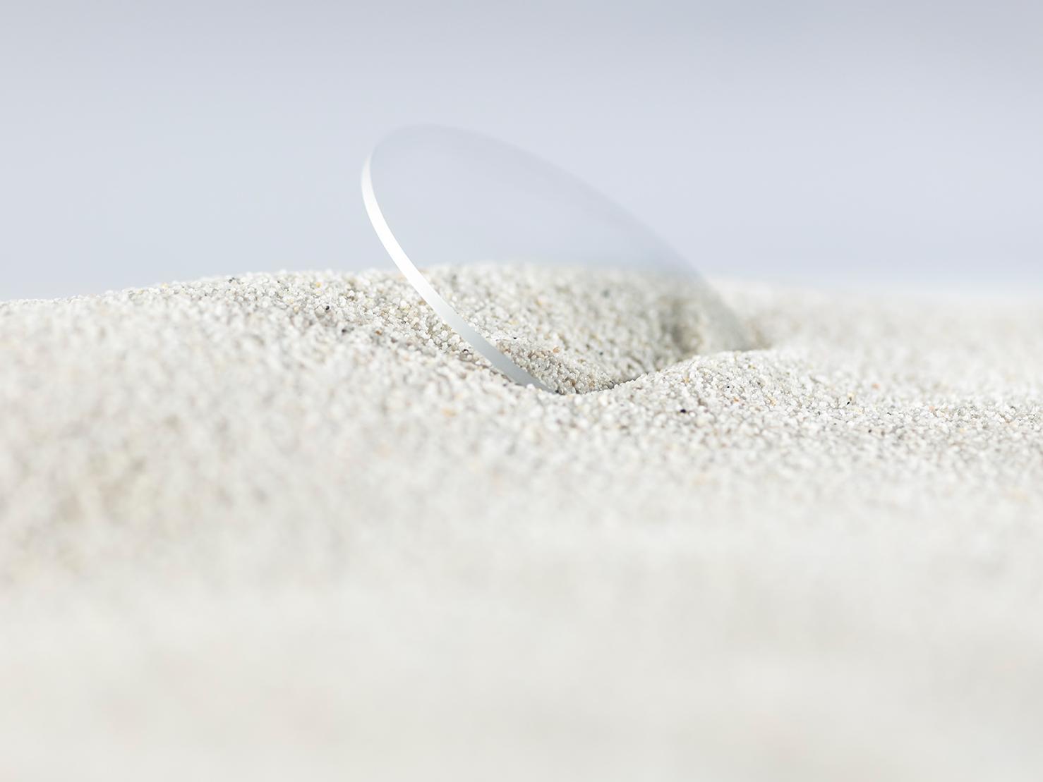 Un lente ZEISS con un recubrimiento duradero se cubre de arena gruesa, pero sigue sin rayarse.