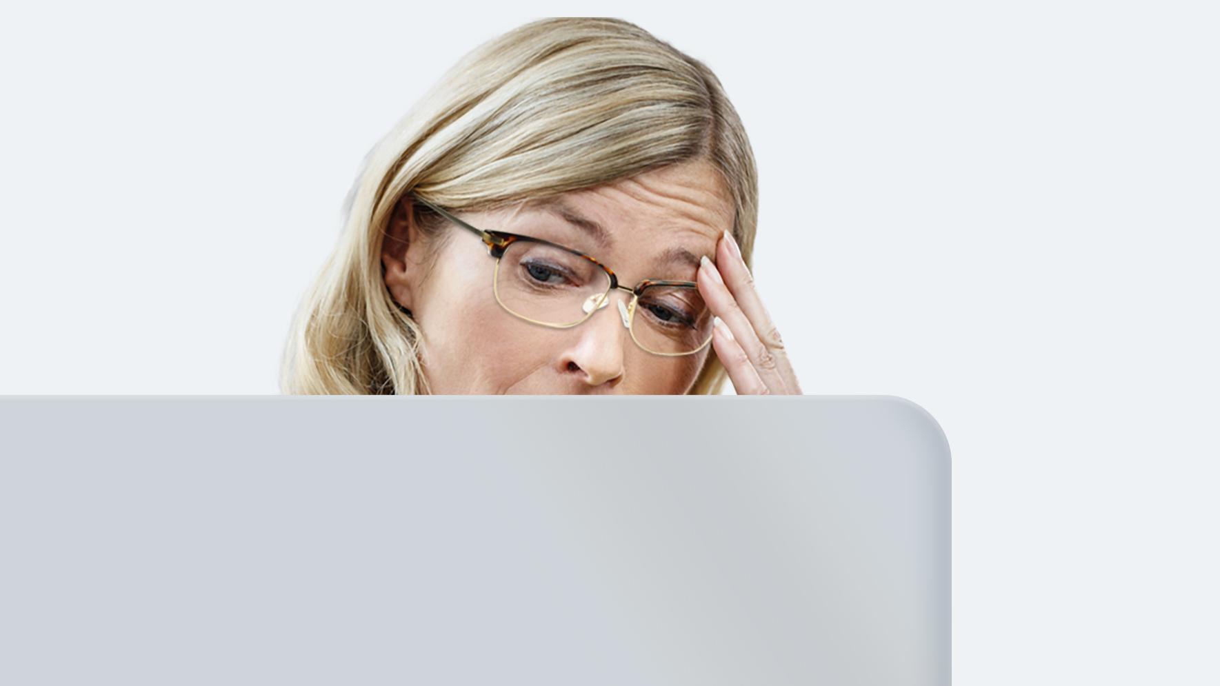 Una mujer de mediana edad con melena larga rubia y lentes de lejos sufre fatiga ocular porque sus lentes no están hechos para mirar una pantalla durante todo el día.