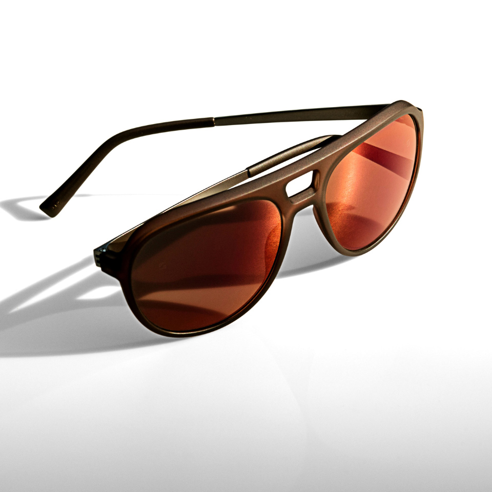 Lentes de sol con efecto espejado en naranja sobre una superficie blanca y luz incidiendo desde el lateral.