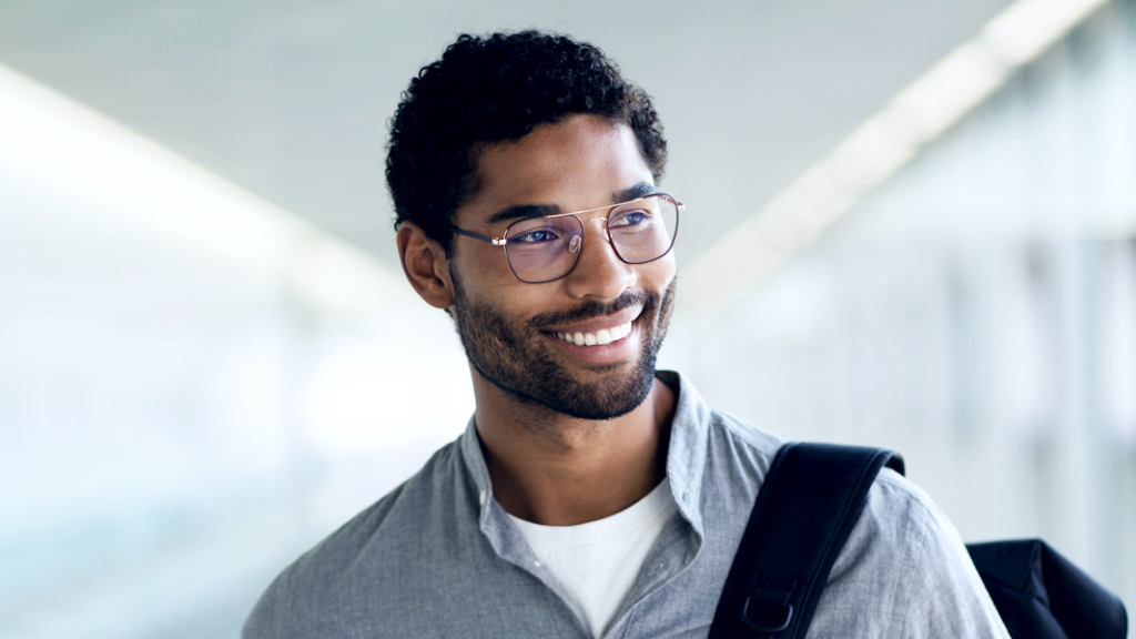 Un joven sonriente con una mochila al hombro usa unos lentes ZEISS Digital SmartLife y mira hacia un lado.